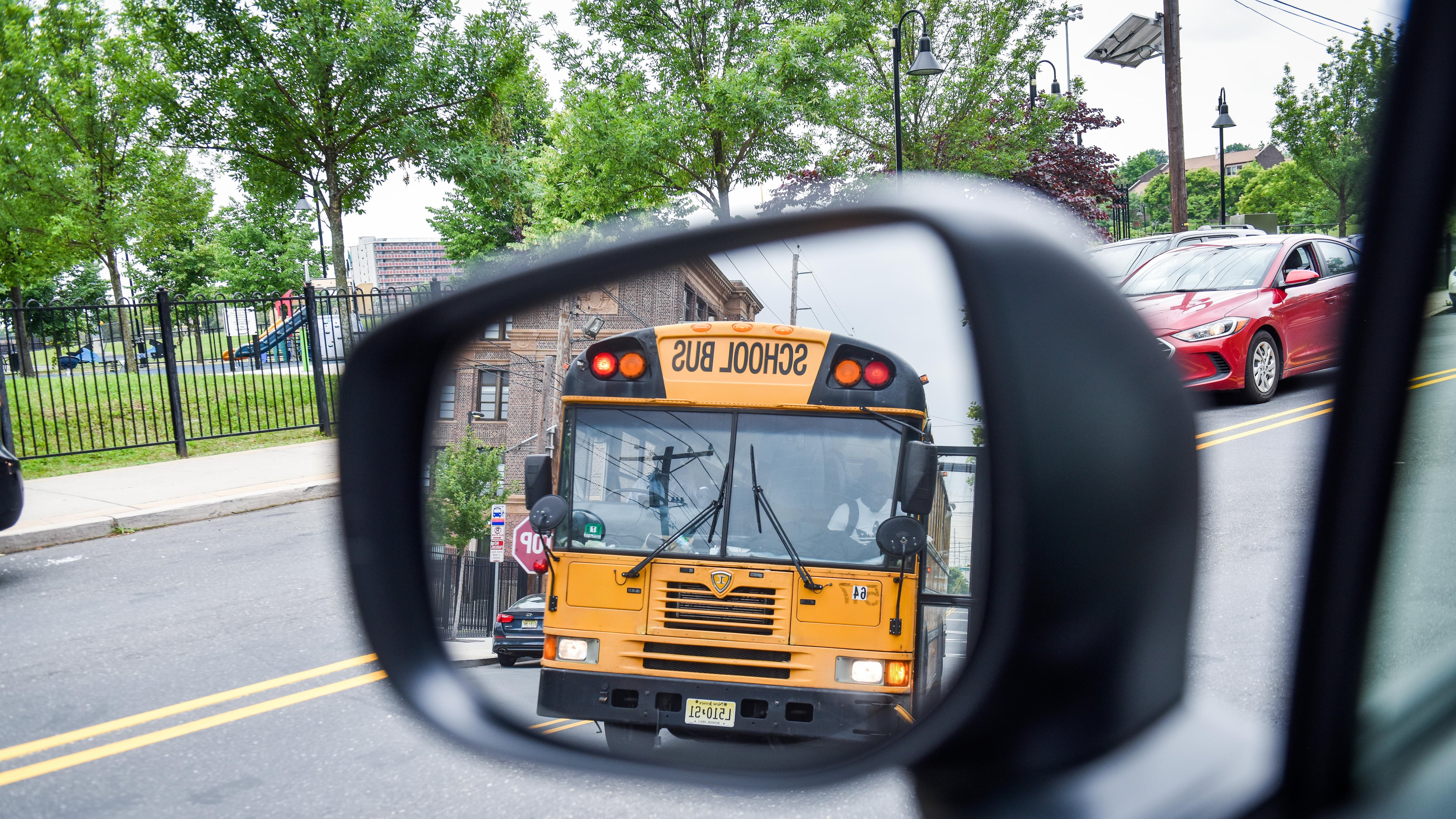 A yellow school bus is seen in the reflection of a car's sideview mirror.