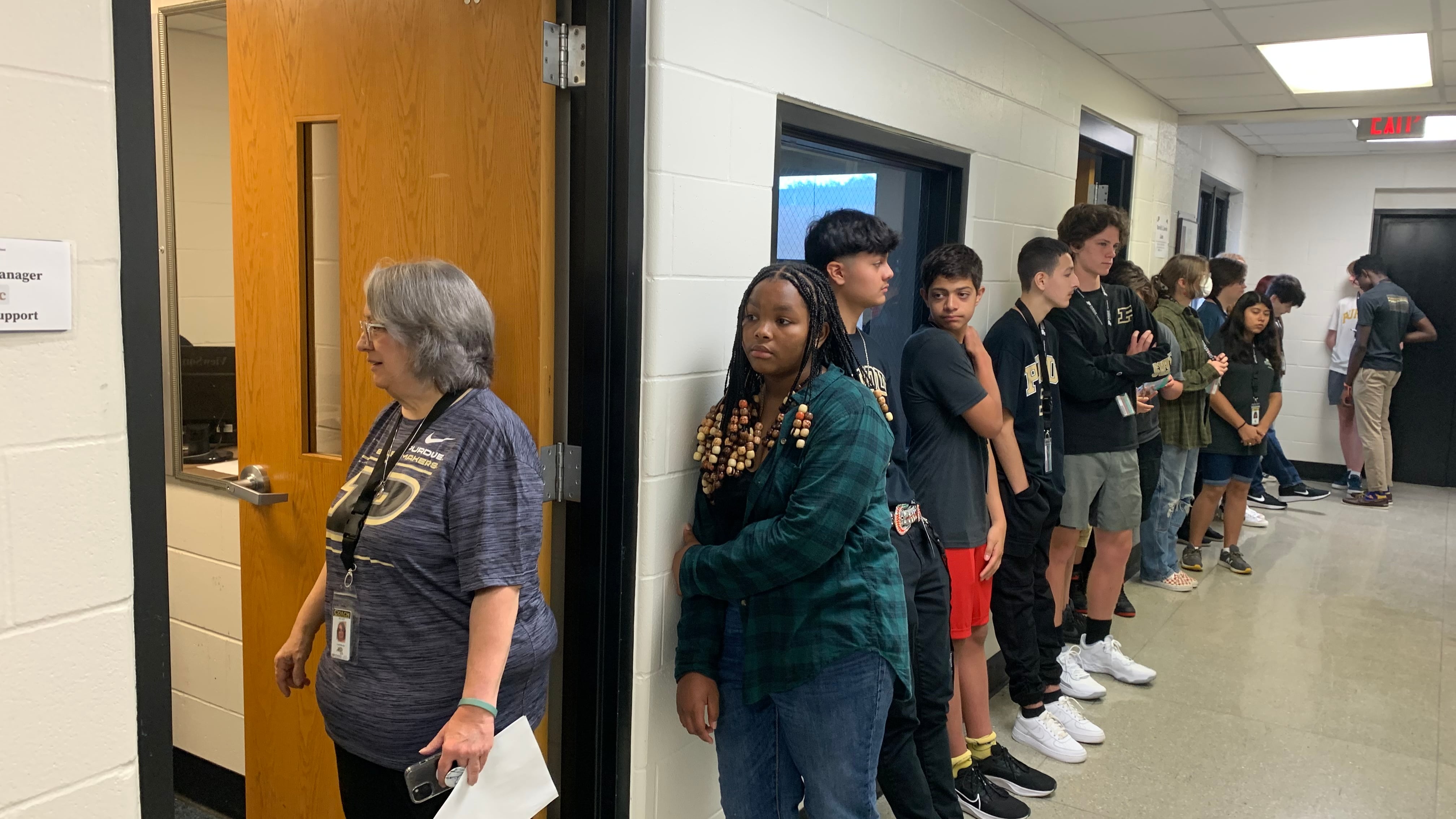 A staff member stands in the doorway next to a long line of high school students.