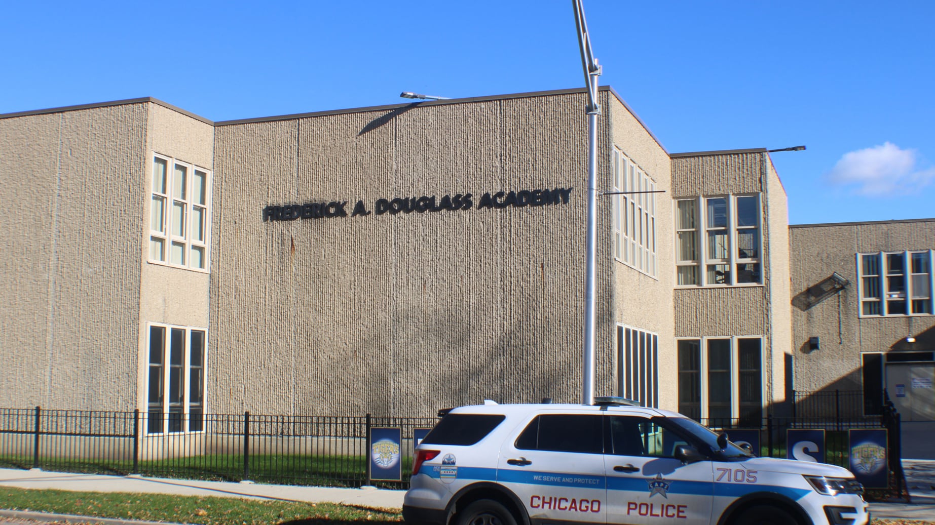 The side of a tan brick school with the name of the school on the side of the building with a Chicago Police car in the foreground.