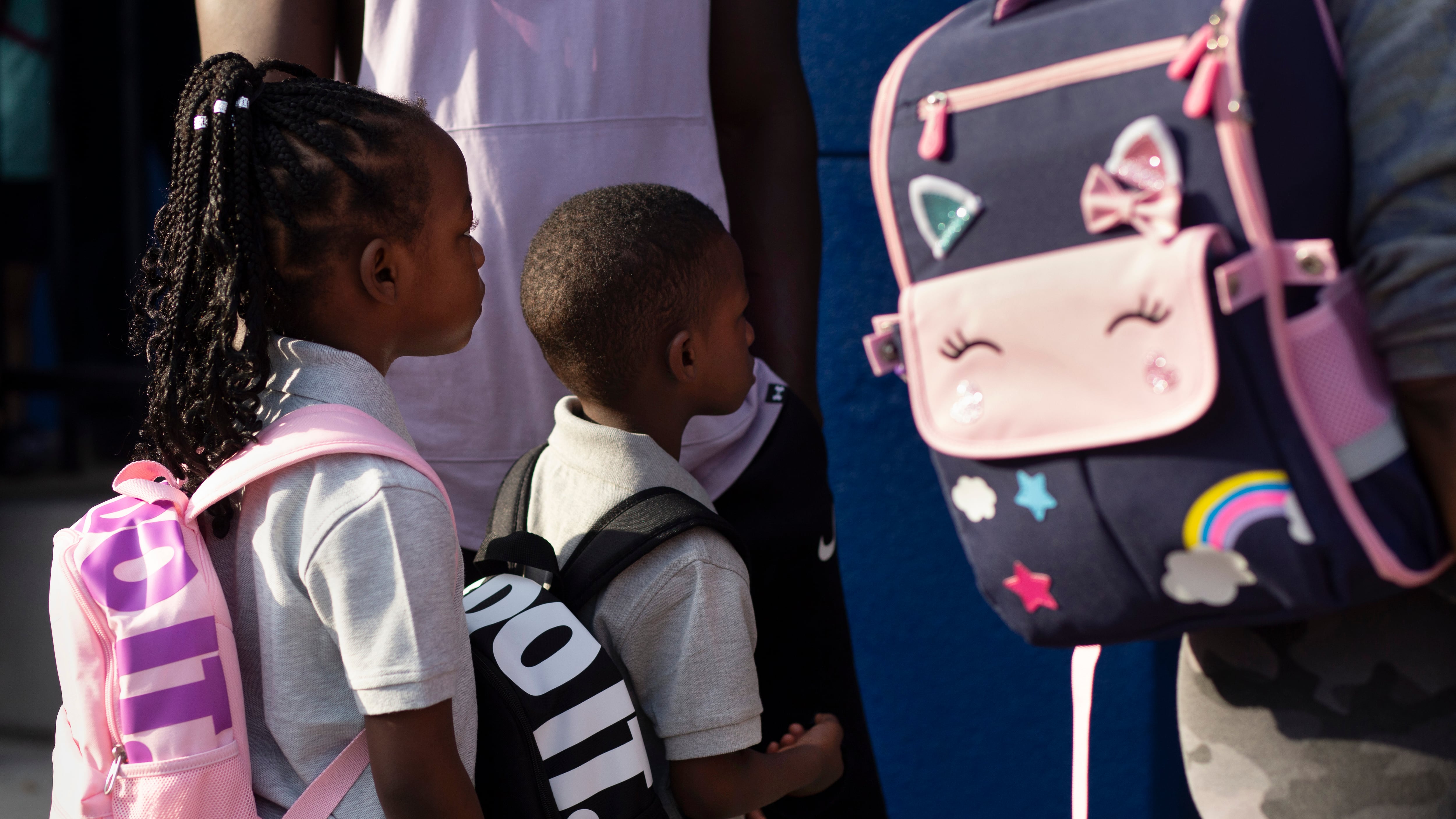 Two students dressed in their best for school and wearing backpacks, stand in line waiting to enter school on the first day.